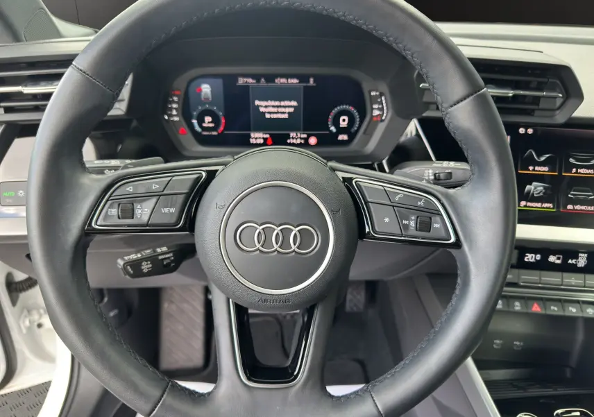 Vue rapprochée du volant cuir noir multifonctions de l'Audi A3 Sportback 2024 avec combiné digital et écran tactile.