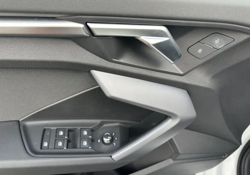 Détail de la porte côté gauche de l'Audi A3 Sportback blanc Arkona 2024 avec commandes électriques et poignée argentée.