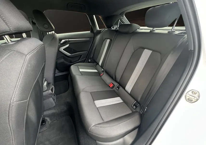 Vue côté gauche de l'intérieur arrière de l'Audi A3 Sportback 2024 blanc Arkona avec sièges tissu noir à bandes grises.
