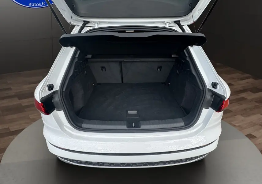 Coffre ouvert vu de l'arrière d'une Audi A3 Sportback 2024 blanc Arkona avec intérieur de coffre noir.