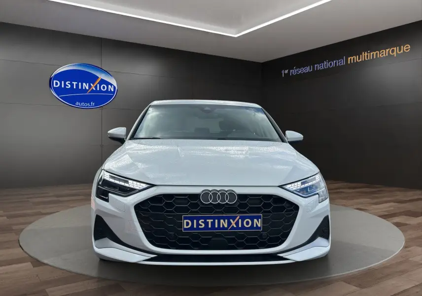 Vue frontale d'une Audi A3 Sportback blanche Arkona 2024 avec calandre hexagonale noire et phares LED distinctifs.