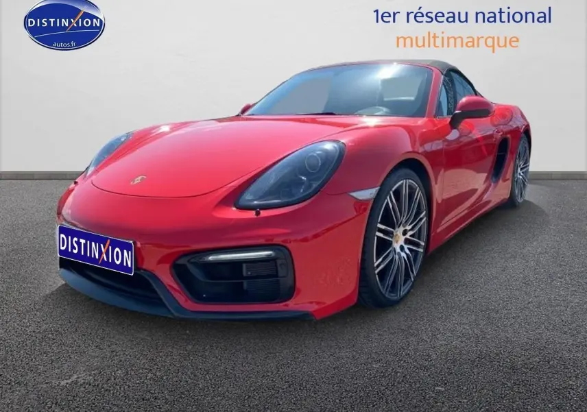 Vue 3/4 avant droite d'une Porsche Boxster rouge (981) avec jantes alu noires et becquet arrière visible.