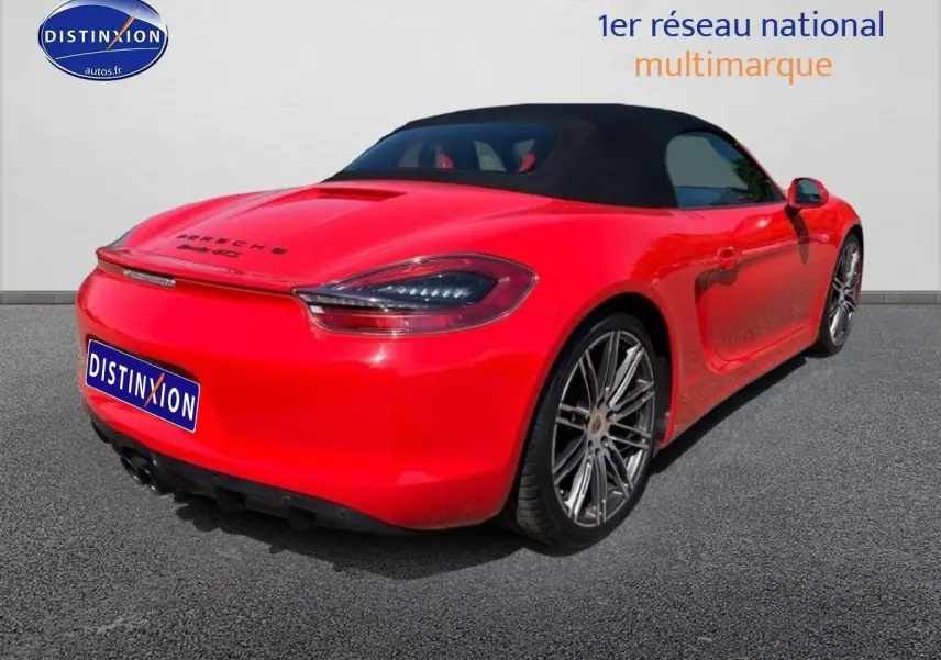 Vue 3/4 arrière droite d'une Porsche Boxster 981 rouge avec capote noire et jantes alu sport