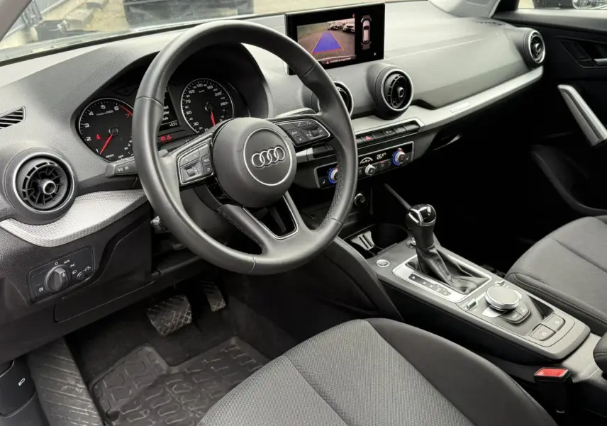 Intérieur de l'Audi Q2 35 TFSI 2023 vu côté conducteur, avec tableau de bord noir et écran caméra de recul.