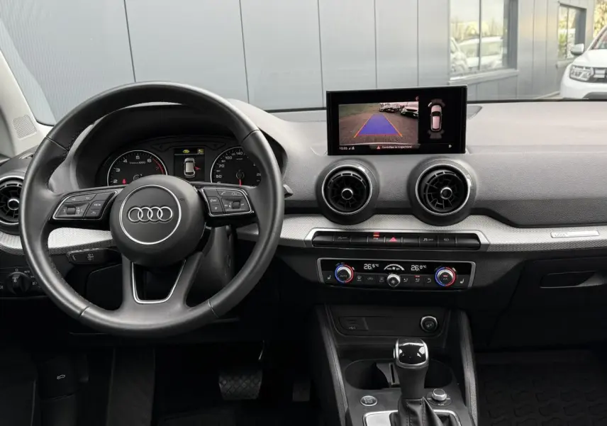 Vue intérieure de l'Audi Q2 35 TFSI S-Line 2023, tableau de bord avec écran caméra de recul et volant multifonction.