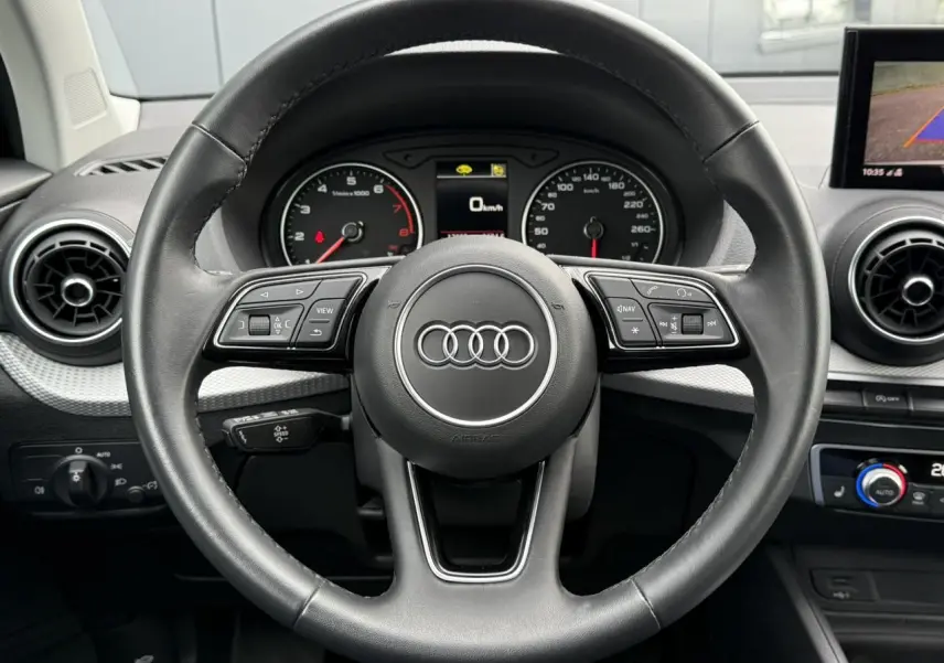 Vue rapprochée du volant noir de l'Audi Q2 35 TFSI 2023 avec commandes intégrées et tableau de bord visible.