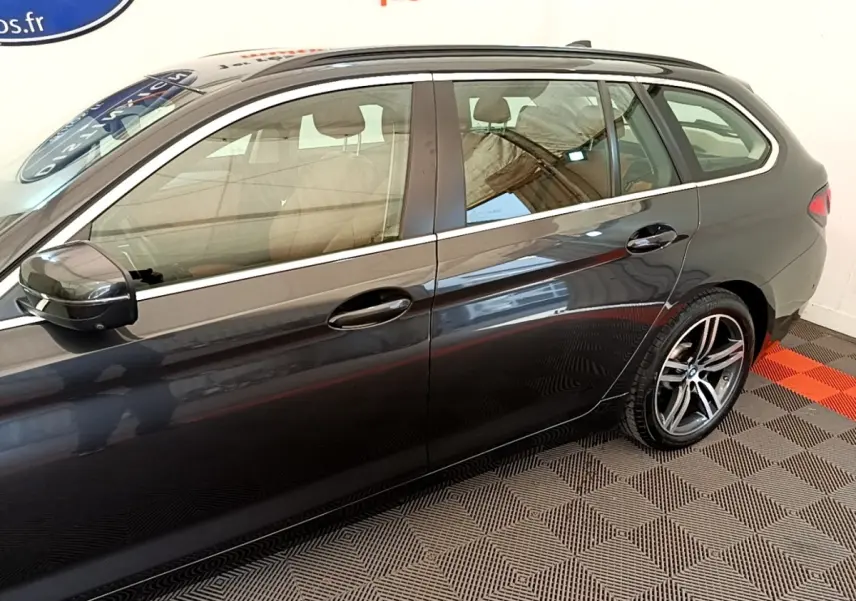 Vue latérale droite d'une BMW Série 5 Touring 530e gris clair avec jantes alliage et rails de toit noirs.