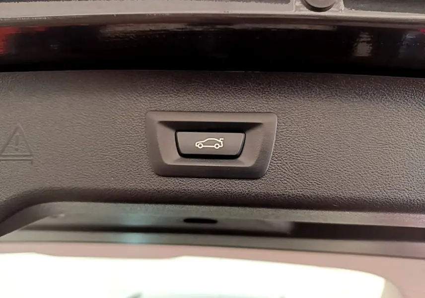 Bouton d'ouverture électrique du coffre sur la partie intérieure du hayon d'une BMW Série 5 Touring gris clair.