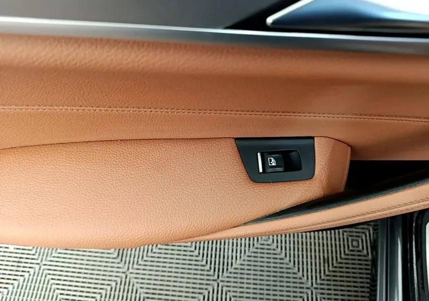 Gros plan sur la commande de lève-vitre intégrée dans la garniture cuir marron clair de la porte avant droite d'une BMW Série 5 Touring.