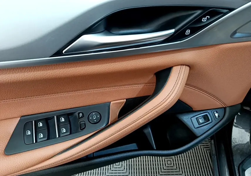 Gros plan sur la porte avant gauche en cuir marron clair avec commandes électriques des vitres et rétroviseurs d'une BMW Série 5 Touring 530e.