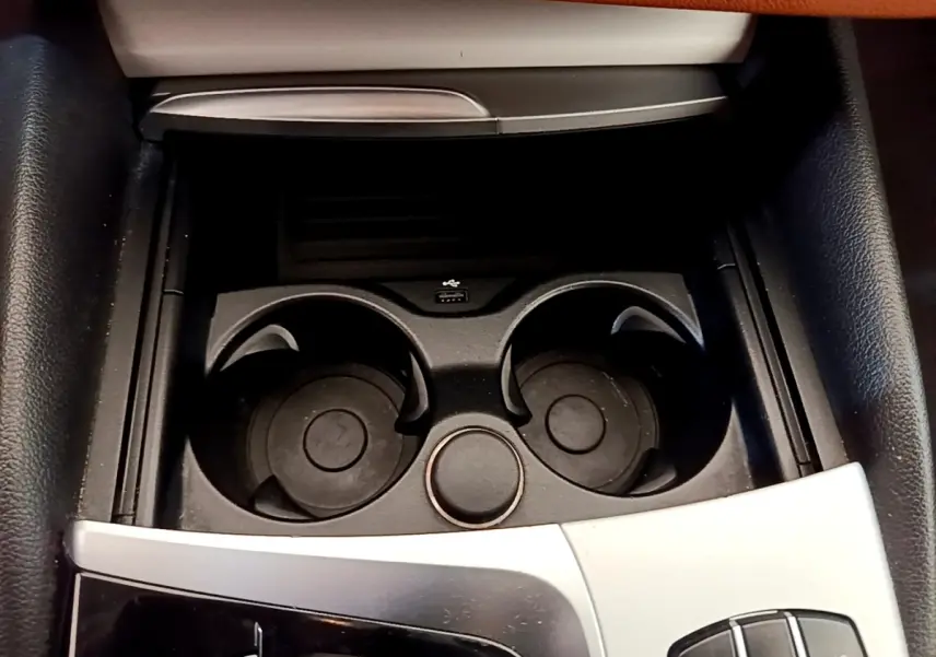 Gros plan sur la console centrale noire avec porte-gobelets et molette de commande dans une BMW Série 5 Touring 530e 2022.