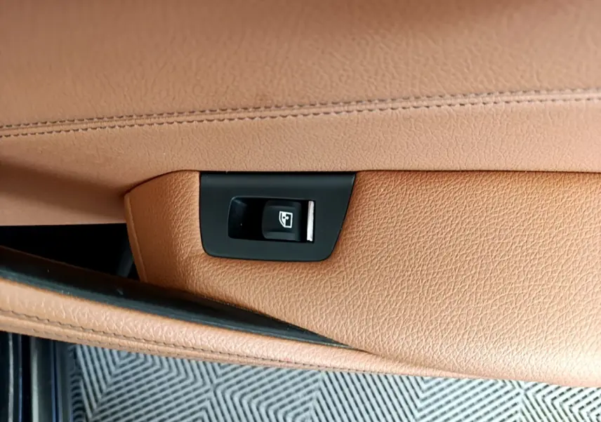 Détail de la commande d'ouverture électrique du coffre sur la garniture cuir marron clair d'une BMW Série 5 Touring 530e 2022.
