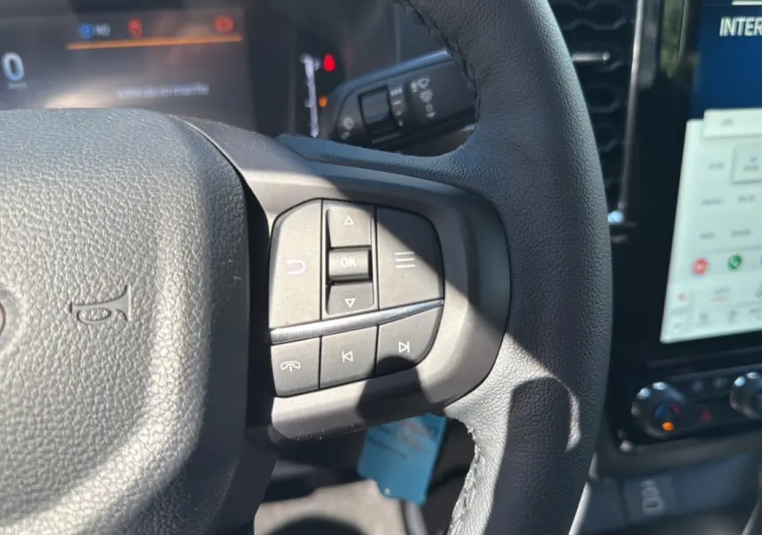 Gros plan sur le volant cuir multifonctions du Ford Ranger blanc glacier, avec commandes audio et écran tactile visible en arrière-plan.