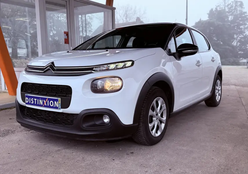 Vue 3/4 avant droite d'une Citroën C3 Société blanche de 2019 avec calandre noire et feux allumés.