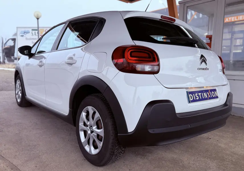 Vue 3/4 arrière droite d'une Citroën C3 Société blanche de 2019 avec feux arrière distinctifs et protections noires.