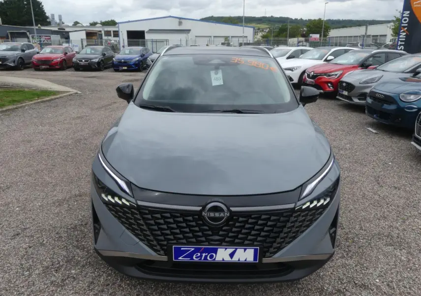 Vue frontale d'un Nissan Qashqai gris métallisé avec calandre noire et feux LED distinctifs sur un parking.