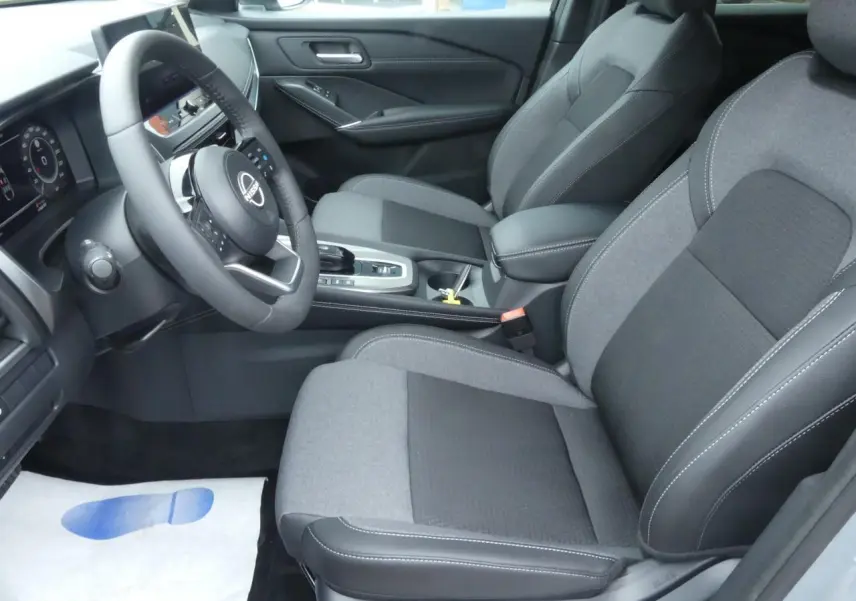 Intérieur avant du Nissan Qashqai 2025, sièges gris tissu et TEP, volant cuir, console centrale avec boîte auto.