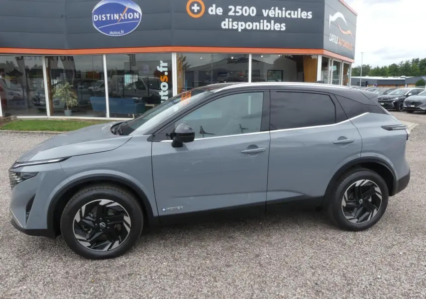 Nissan Qashqai 2025 gris métallisé, vue profil côté gauche, toit noir bi-ton et jantes alliage noires.