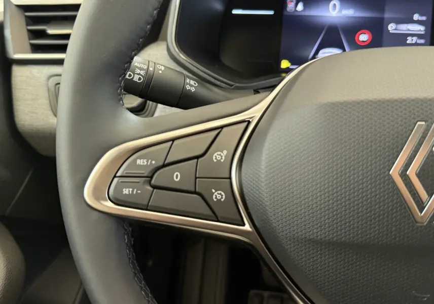 Gros plan sur le côté gauche du volant cuir noir de la Renault Clio 2025 avec commandes de régulateur de vitesse et tableau de bord numérique.