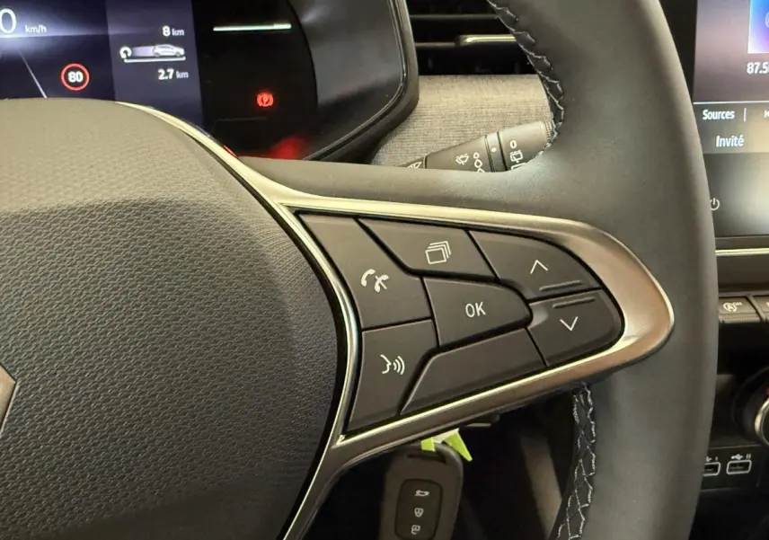 Gros plan sur le volant cuir noir de la Renault Clio 2025 avec commandes multifonctions et affichage numérique partiel.