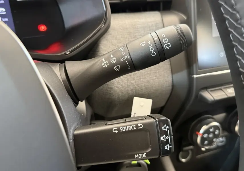 Gros plan sur les commandes au volant de la Renault Clio 2025, avec levier d'essuie-glace et boutons multimédia visibles.