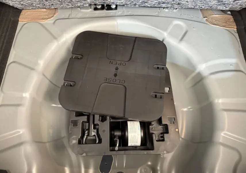 Compartiment de rangement sous le plancher du coffre de la Renault Clio noire, montrant le kit de réparation pneus.