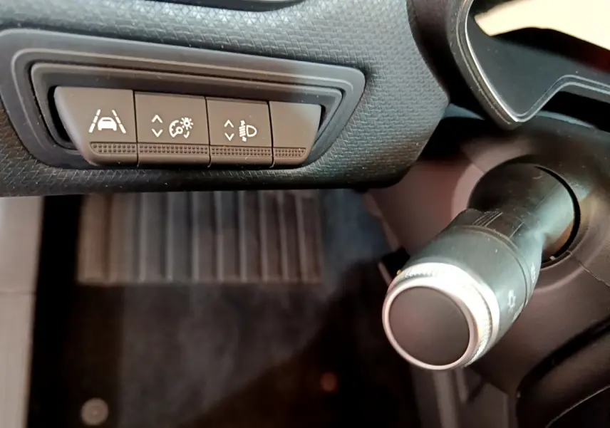 Gros plan sur les commandes d'assistance et réglage des phares côté gauche du tableau de bord noir de la Renault Clio Business blanche.