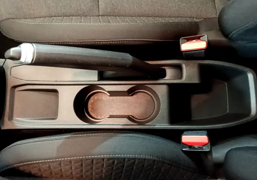 Vue plongeante sur la console centrale noire de la Renault Clio Business avec frein à main manuel et ceintures rouges.