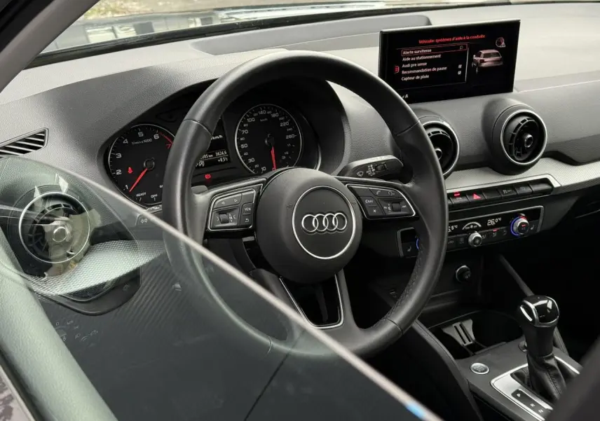 Intérieur de l'Audi Q2 35 TFSI 2023 vu côté conducteur, tableau de bord noir avec volant multifonction et écran central.