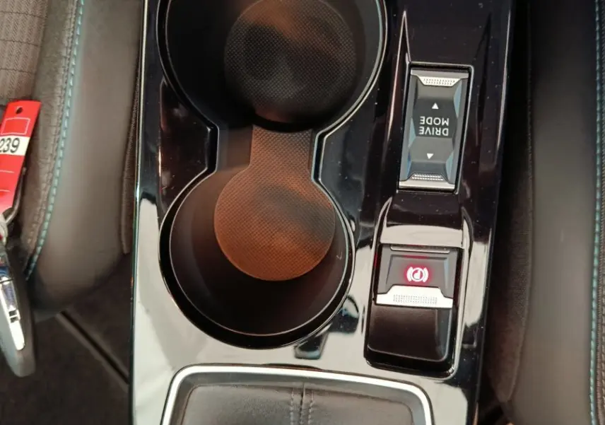 Vue plongeante sur la console centrale noire brillante de la Peugeot 208 avec porte-gobelets et commandes Drive Mode et frein électrique.