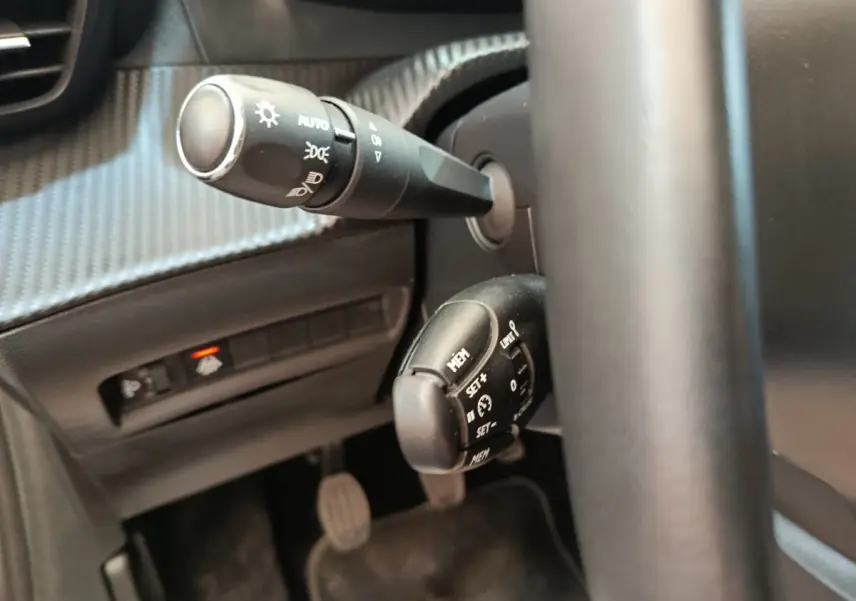 Gros plan sur la commande de régulateur de vitesse et les commandes d’éclairage derrière le volant noir du Peugeot 208.