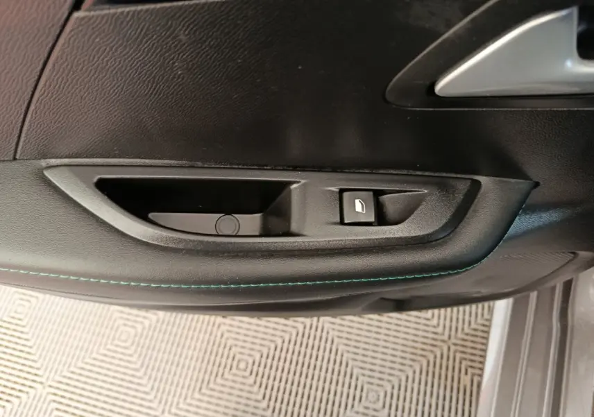 Poignée intérieure de porte côté conducteur de Peugeot 208 2020 avec bouton de verrouillage et surpiqûres bleues.