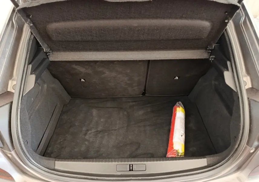 Coffre ouvert vu de dessus d’une Peugeot 208 2020, moquette noire avec triangle de signalisation rangé à droite.