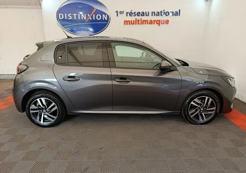 Vue latérale droite d'une Peugeot 208 gris foncé 2020 avec jantes alliage et vitres teintées en intérieur showroom.