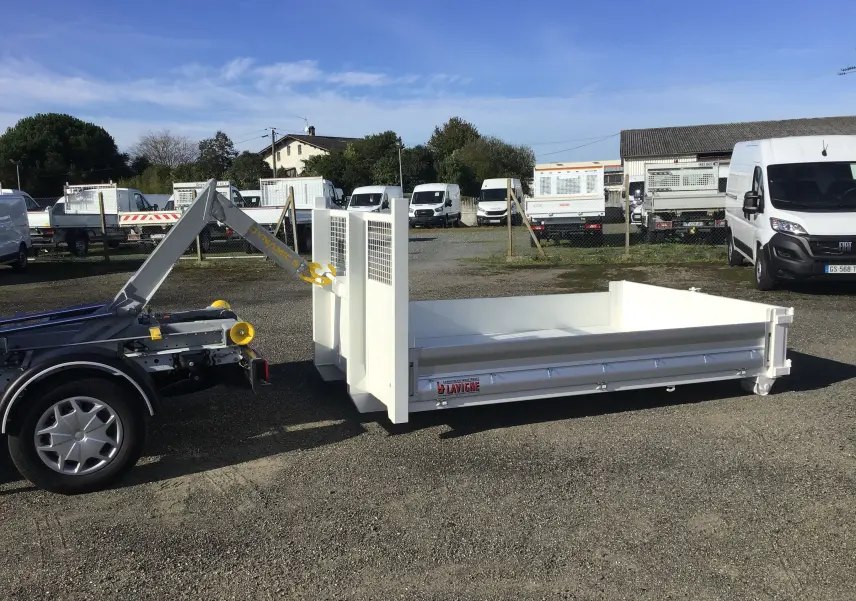 Vue latérale droite d'un Ford Transit blanc avec bras polybenne et benne arrière 3m20 ouverte sur parking.
