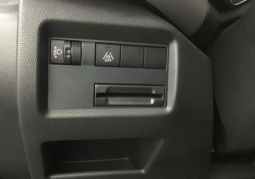 Gros plan sur les commandes de réglage des phares et d'aide à la conduite du tableau de bord noir d'une Citroën C5 Aircross gris Artense.