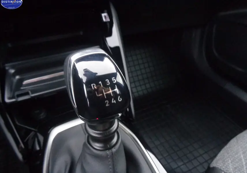 Le levier de vitesses manuel noir brillant de la Peugeot 2008 1.2 PureTech, intérieur sombre avec tapis caoutchouc.
