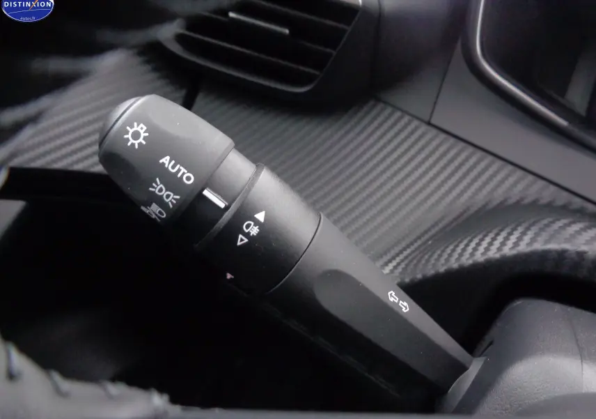 Gros plan sur la commande des feux automatique dans l'habitacle au design carbone du Peugeot 2008 bleu Vertigo 2023.