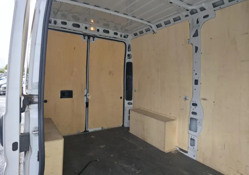 Intérieur du fourgon Opel Movano blanc vu de l'arrière avec panneaux latéraux et plancher en bois clair.