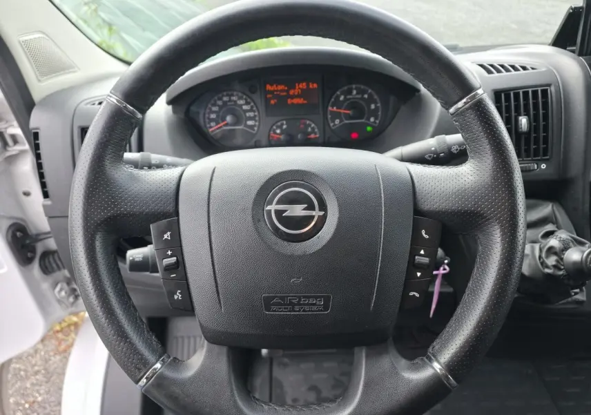 Volant noir perforé avec logo Opel au centre, tableau de bord numérique et levier de vitesses manuel visible côté droit.