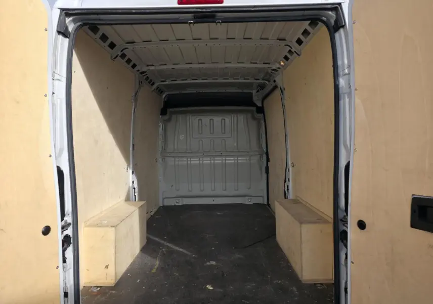 Vue arrière intérieure du fourgon blanc Opel Movano avec panneaux latéraux en bois et plancher noir.