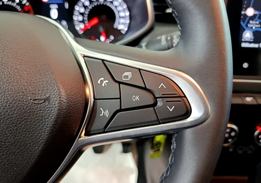 Gros plan sur les commandes multifonctions du volant cuir noir de la Renault Clio Business blanche, tableau de bord en arrière-plan.