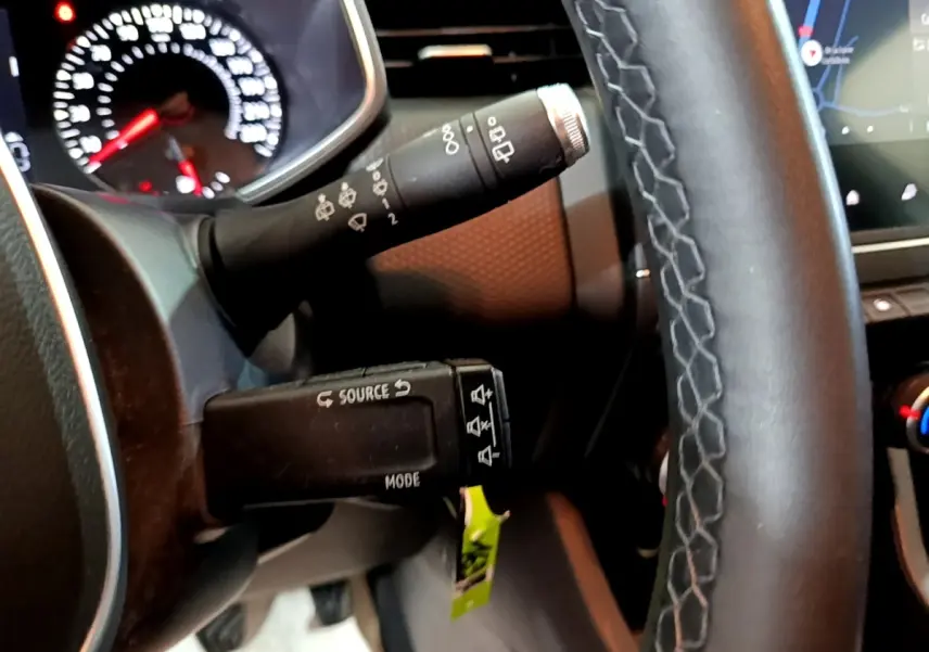 Gros plan sur le volant cuir synthétique et les commandes au volant d'une Renault Clio blanche, avec tableau de bord et écran tactile visibles.