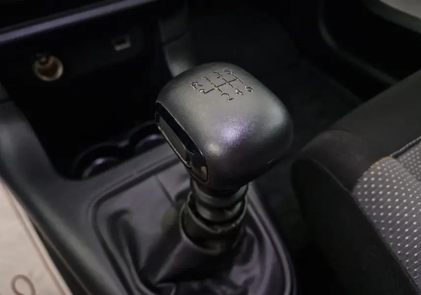 Gros plan sur le levier de vitesses manuel noir de la Citroën C3 Société blanche, intérieur sombre avec siège tissu gris à motifs.