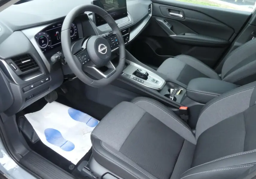 Intérieur du Nissan Qashqai 2025 vu côté conducteur, sellerie mixte gris et console centrale moderne avec volant multifonction.