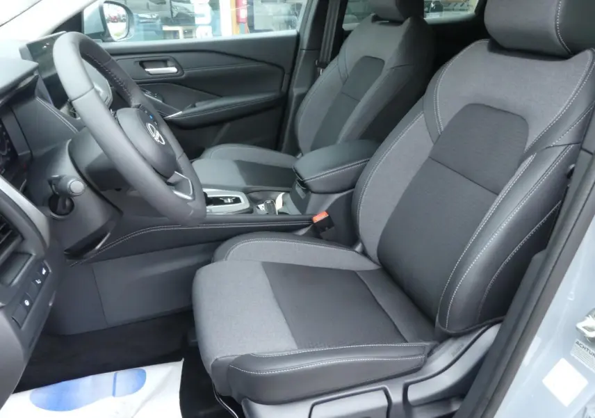 Vue intérieure côté conducteur du Nissan Qashqai 1.5 e-Power 2025 avec sièges gris en tissu et accoudoir central.