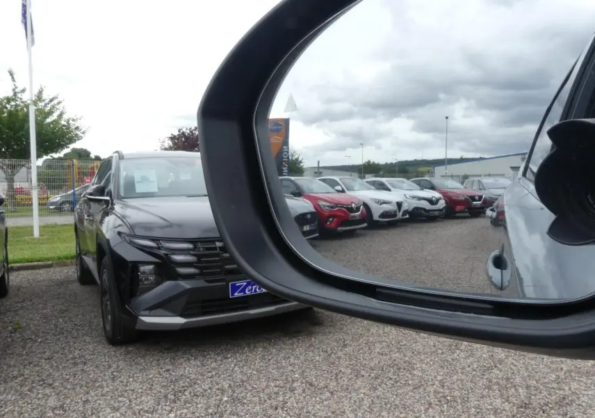 Vue en miroir du rétroviseur droit montrant un Nissan Qashqai gris métallisé de face sur un parking.