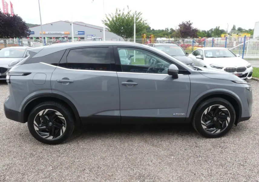 Profil côté gauche d'un Nissan Qashqai 1.5 e-Power gris métallisé avec jantes alliage 18 pouces et vitres teintées.