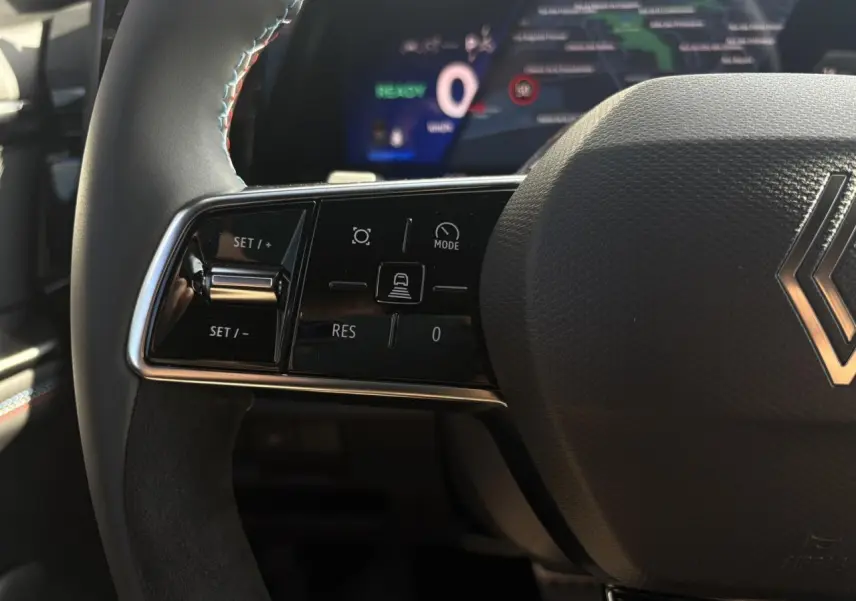 Gros plan sur le volant Alcantara du Renault Rafale E-Tech avec commandes multifonctions et surpiqûres tricolores visibles.