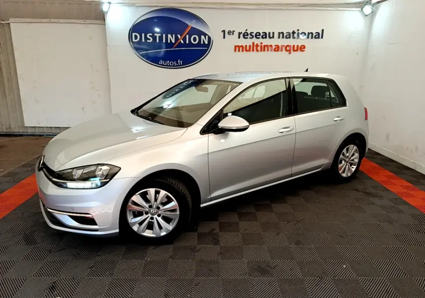 Volkswagen Golf 1.6 TDI gris clair vue 3/4 avant droit dans un showroom avec logo Distinxion en arrière-plan.